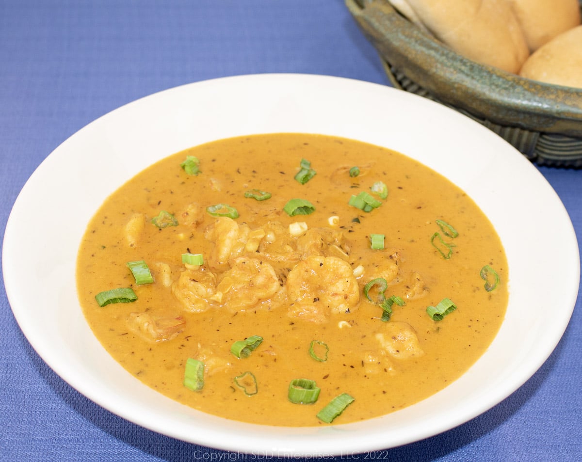 corn and shrimp bisque in a white bowl with green onion garnish