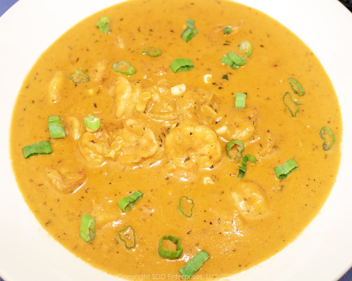 corn and shrimp bisque in a white bowl with green onion garnish