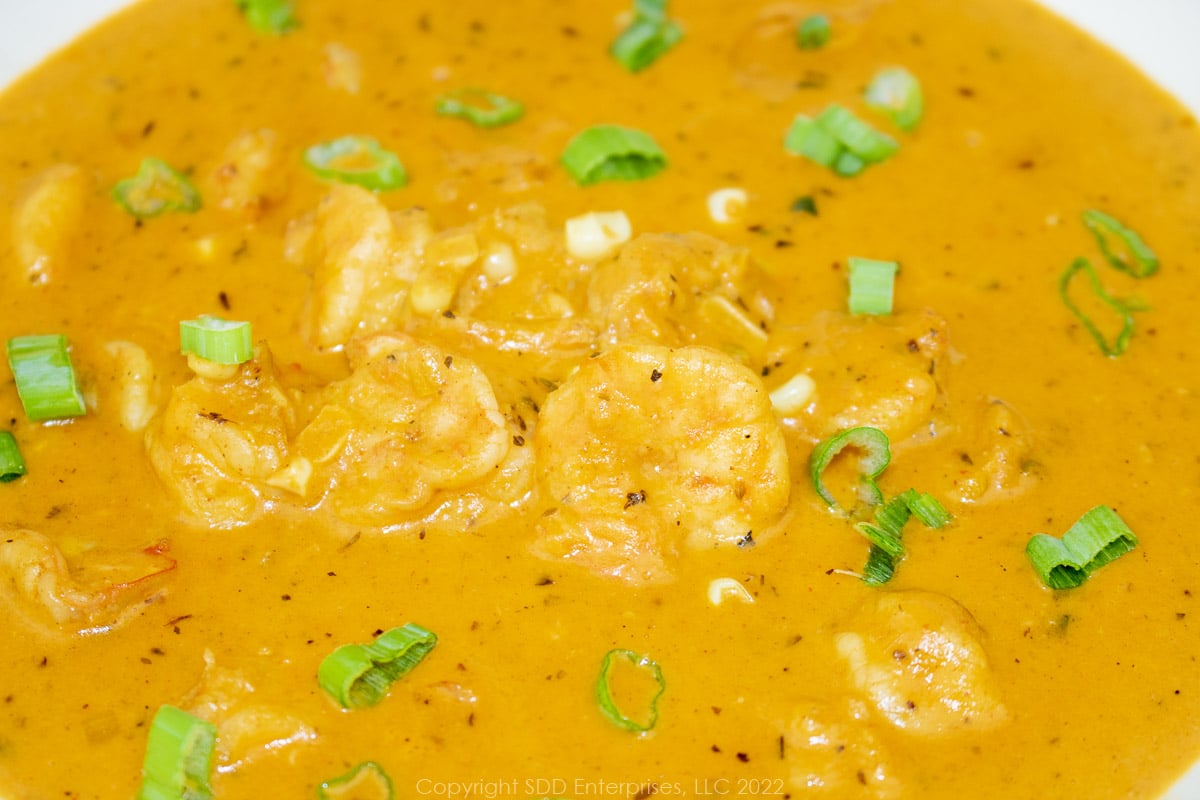 corn and shrimp bisque in a white bowl with green onion garnish