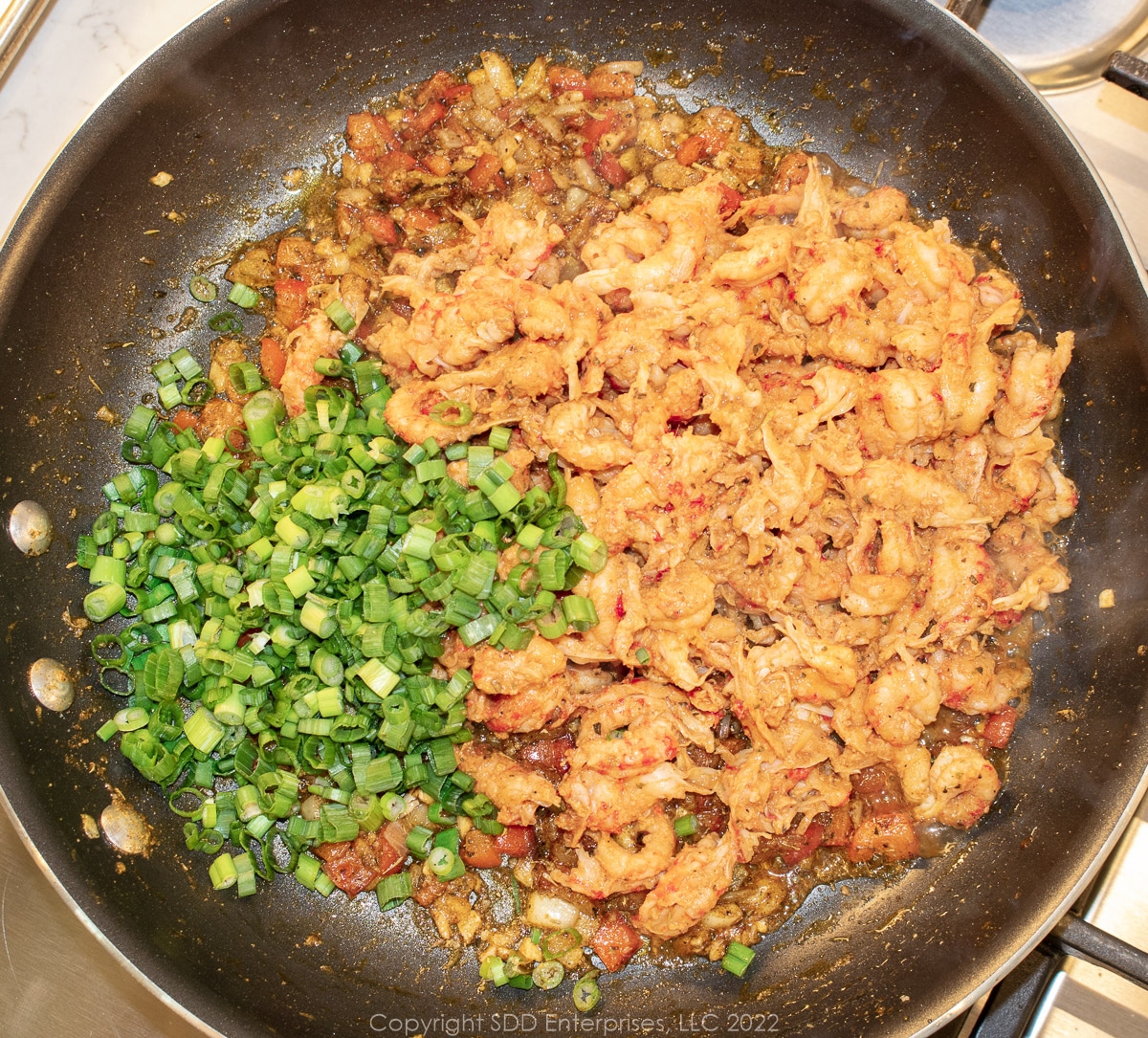 crawfish tails and green onions added to sauteed vegetables in a sauté pan