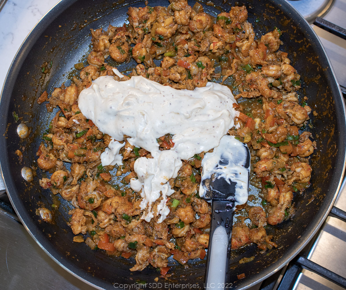mayonnaise and other ingredients added to a sauté pan of crawfish tails and sautéed vegetables