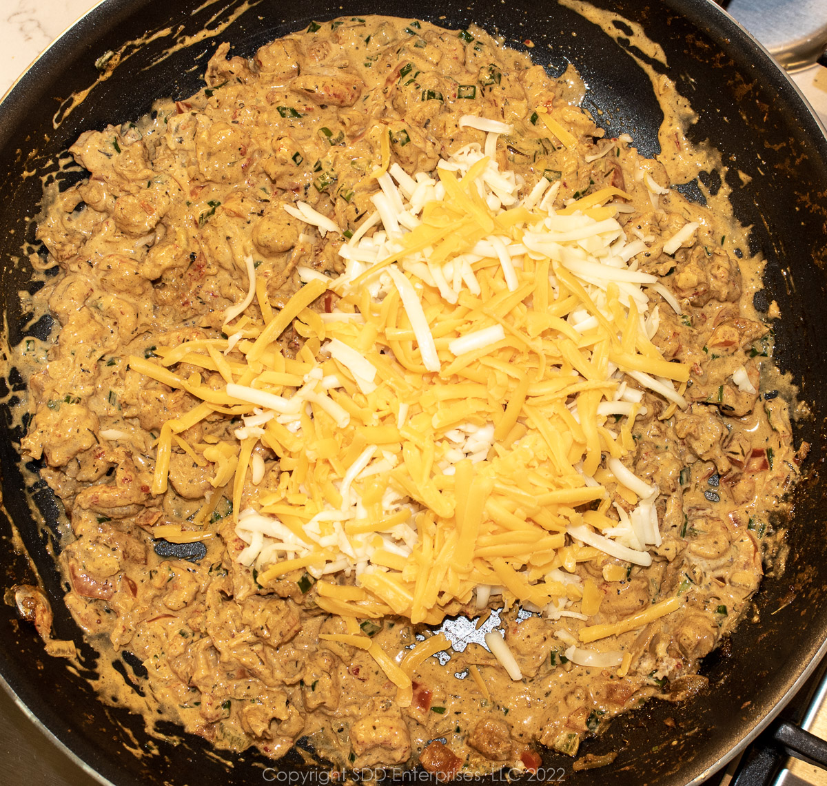 grated cheese with crawfish mix in a sauté pan