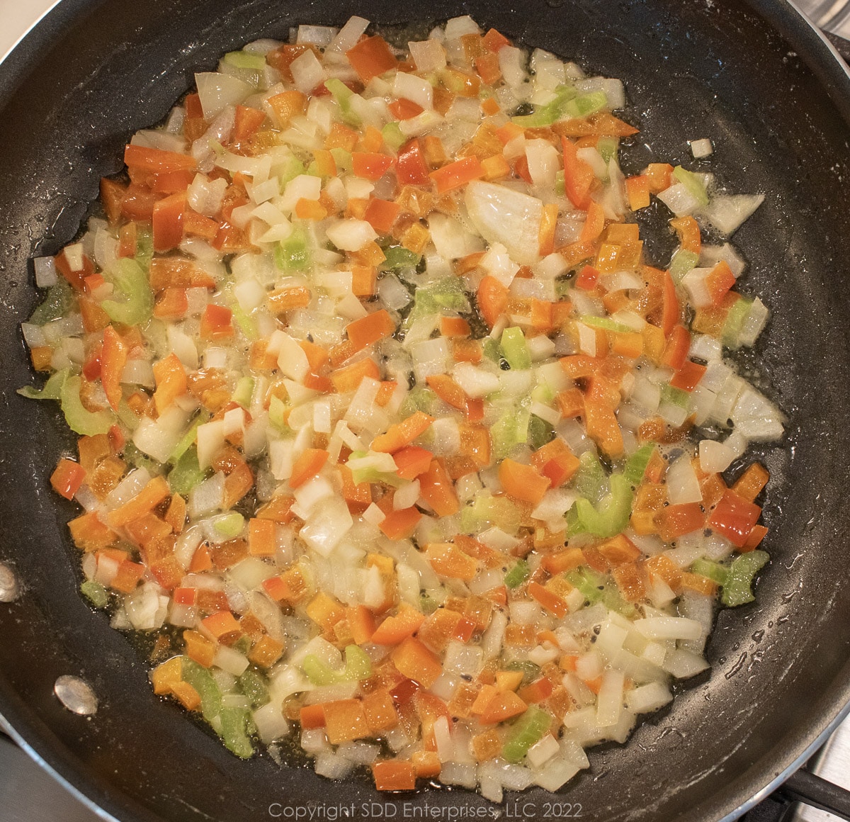onions, peppers and celery sautéing in butter in a sauté pan