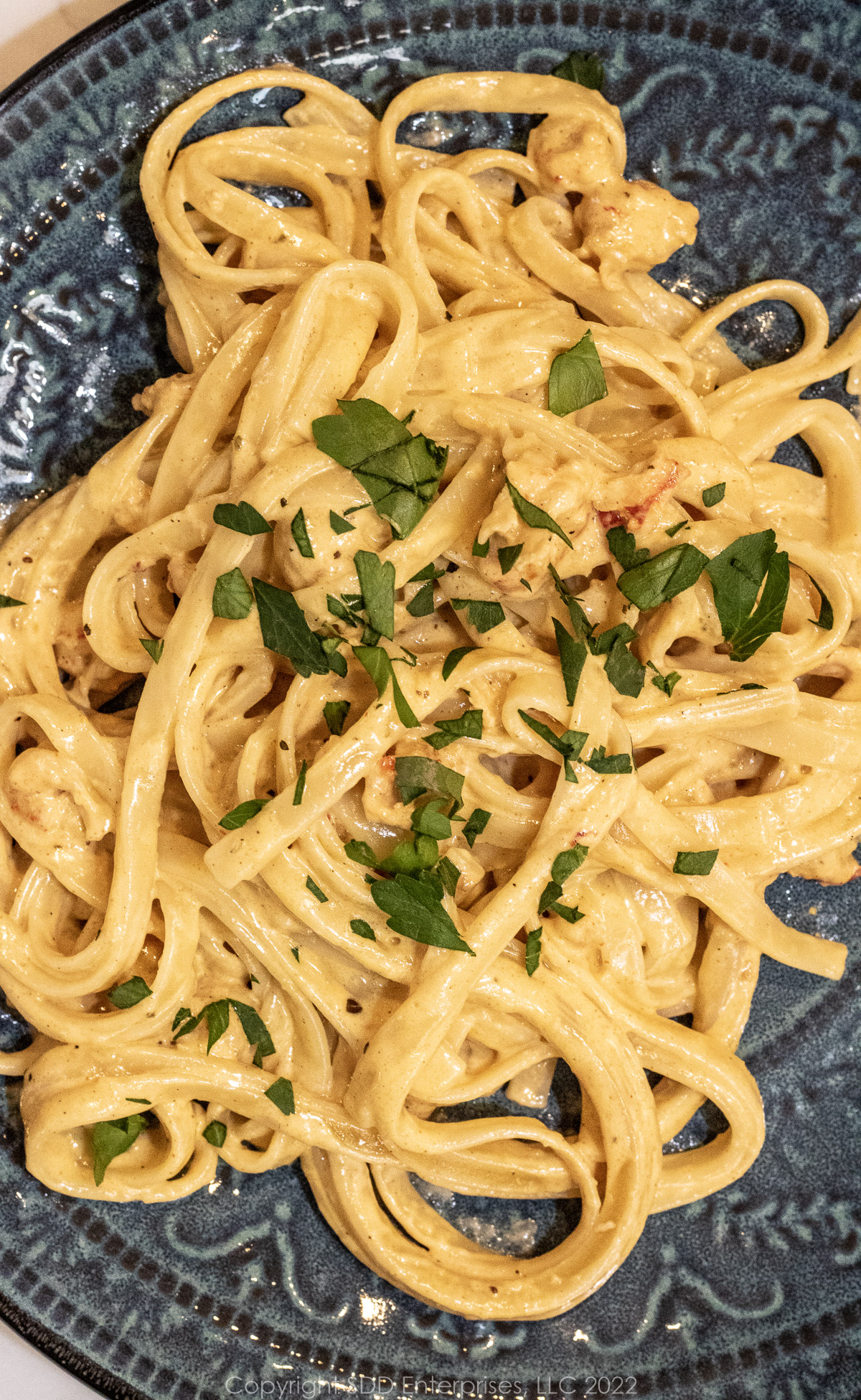 Fettuccini in alfredo sauce with crawfish and parsley garnish on a blue green plate. 