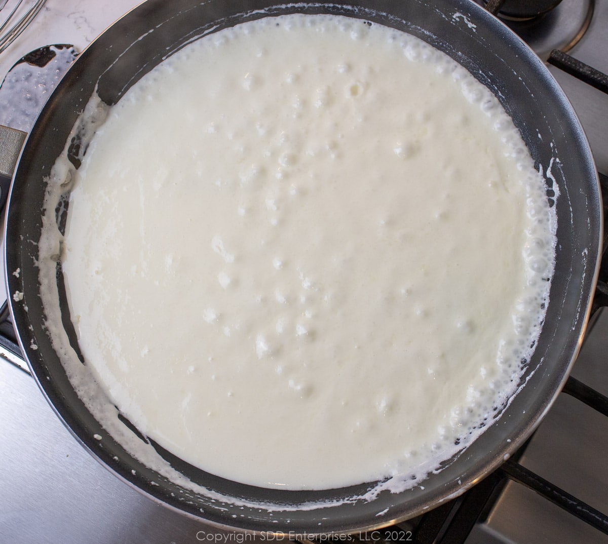 simmering alfredo sauce in a sauté pan