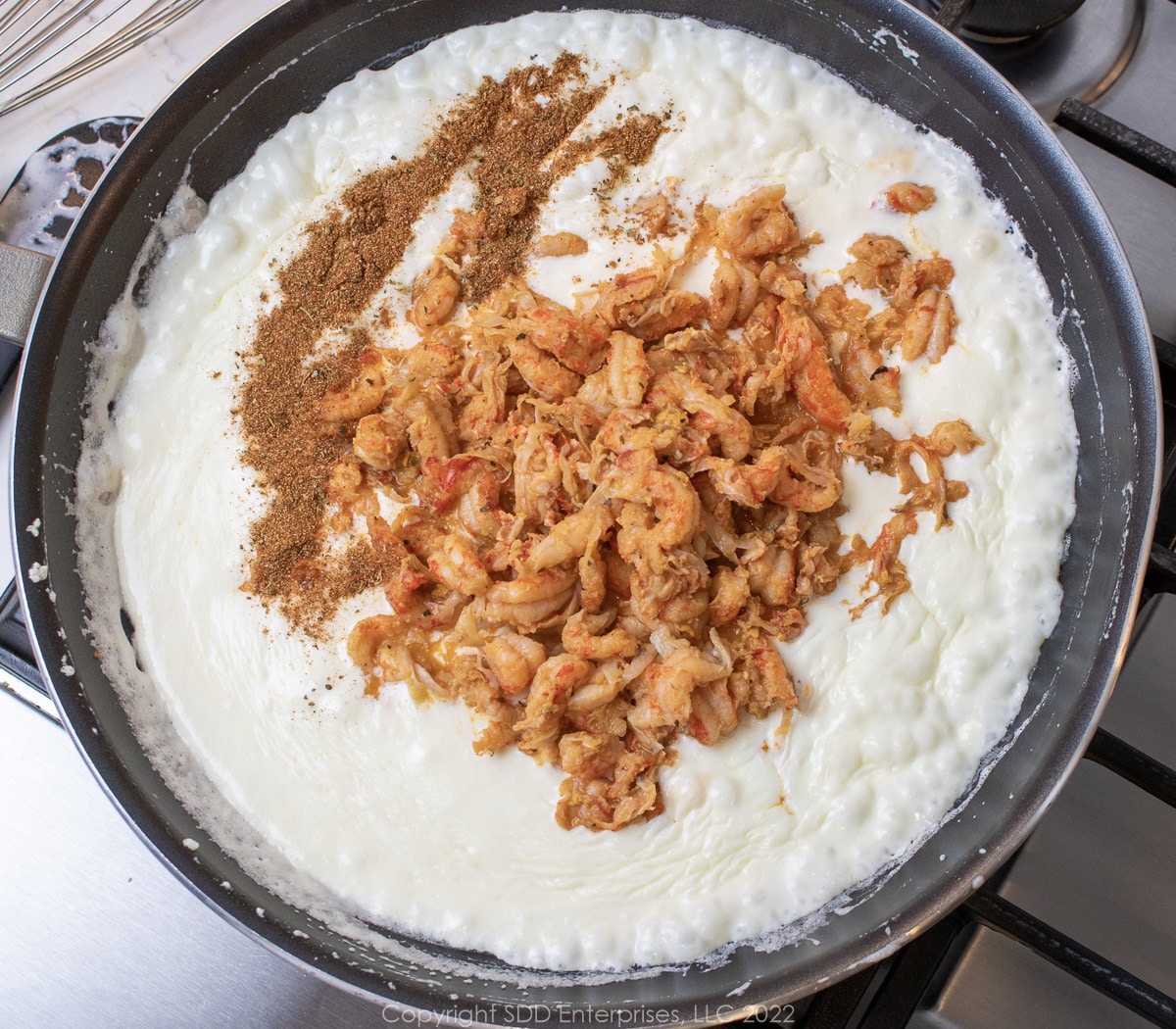 crawfish tails and seasoning added to alfredo sauce in a sauté pan