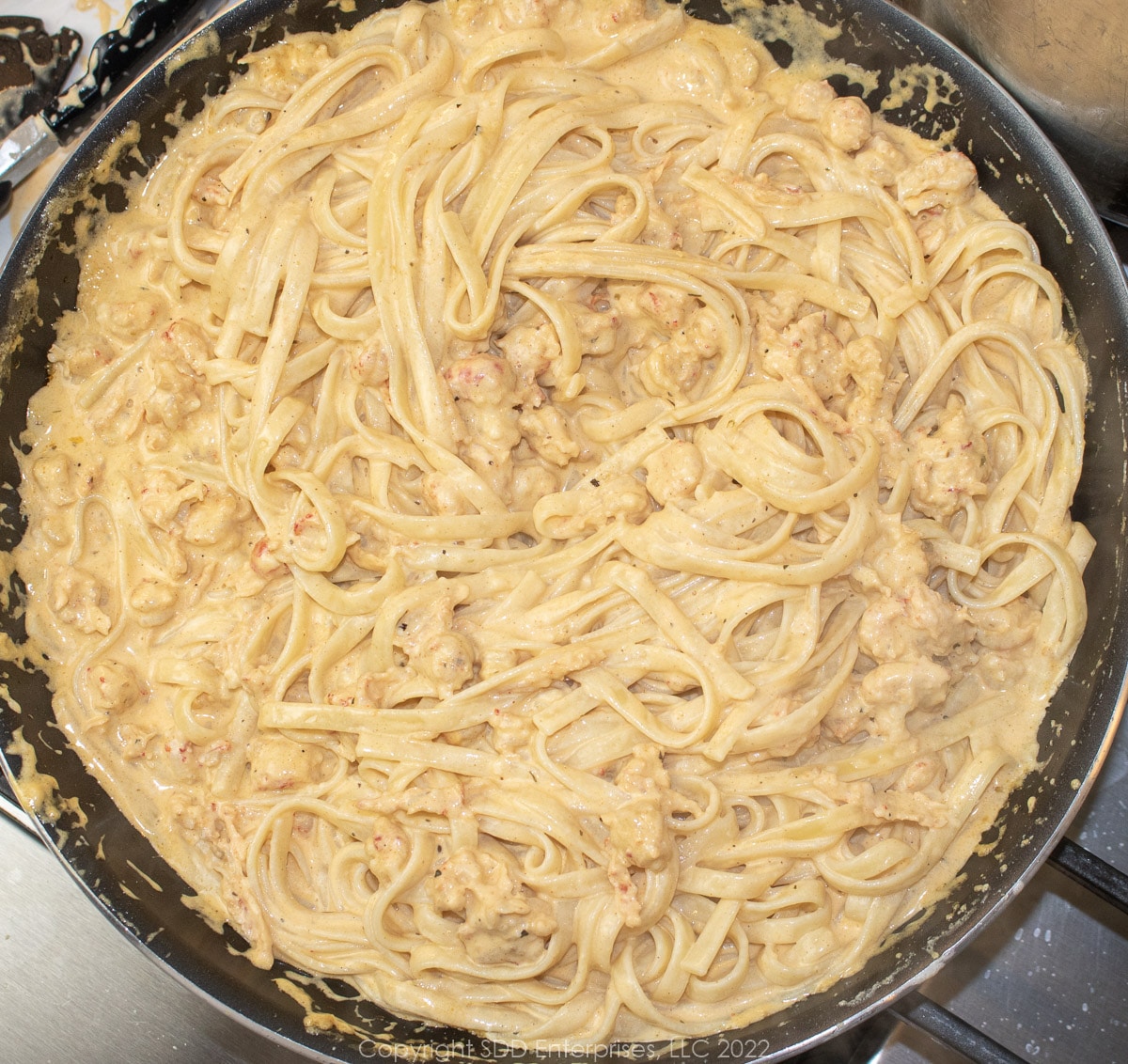 fettuccini added to alfredo sauce with crawfish tails in a sauté pan