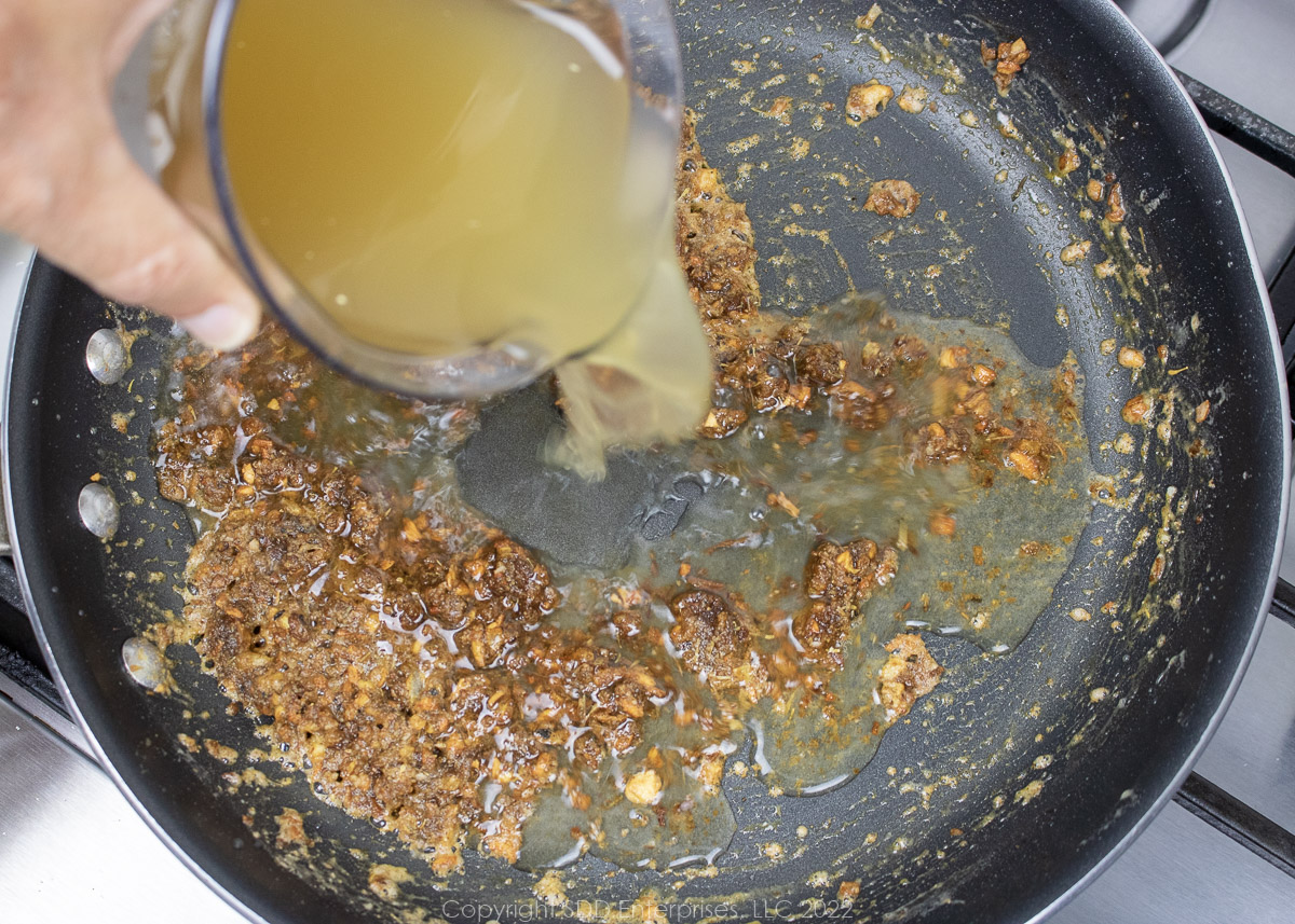 stock being added to roux and veggies in a sauté pan