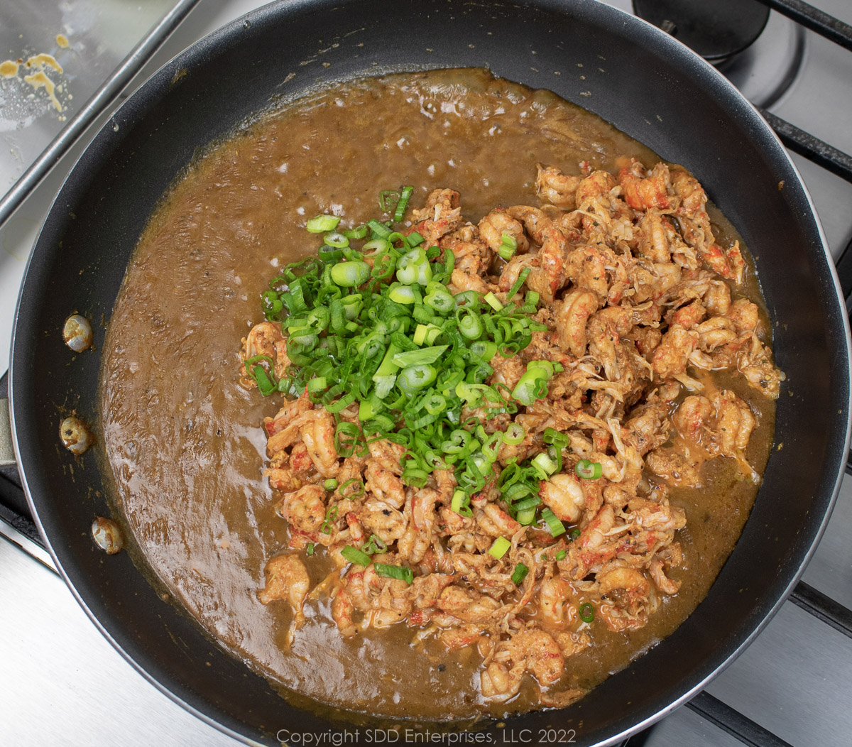 crawfish tails and green onions are added to brown sauce in a sauté pan