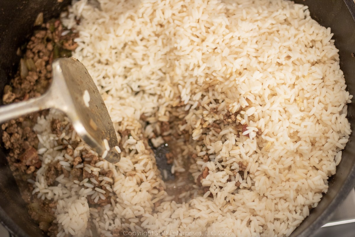 cooked rice added to seasoned ground meats and seasonings in a Dutch oven