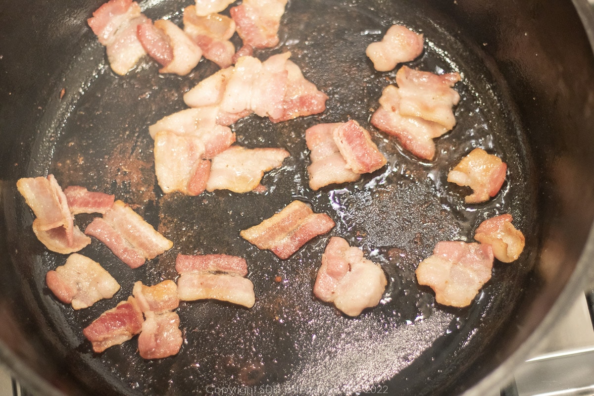 pieces of bacon frying in a Dutch oven