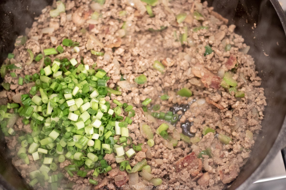 green oinions added to browning meats in a Dutch oven