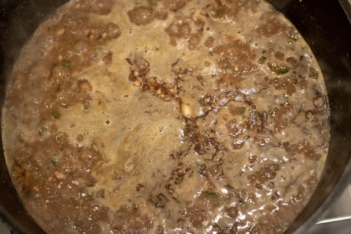 beef stock combined with simmering meats and seasonings in a Dutch oven