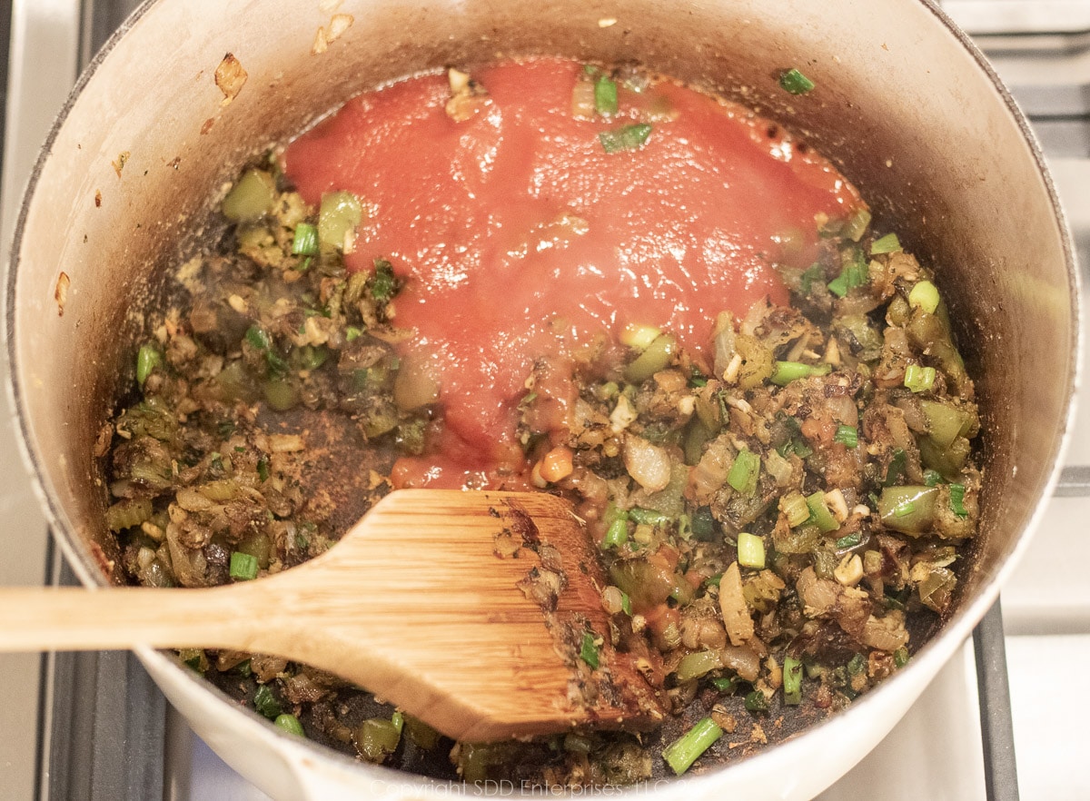 tomatoes and tomato sauce mixed into sautéed vegetable in a Dutch oven