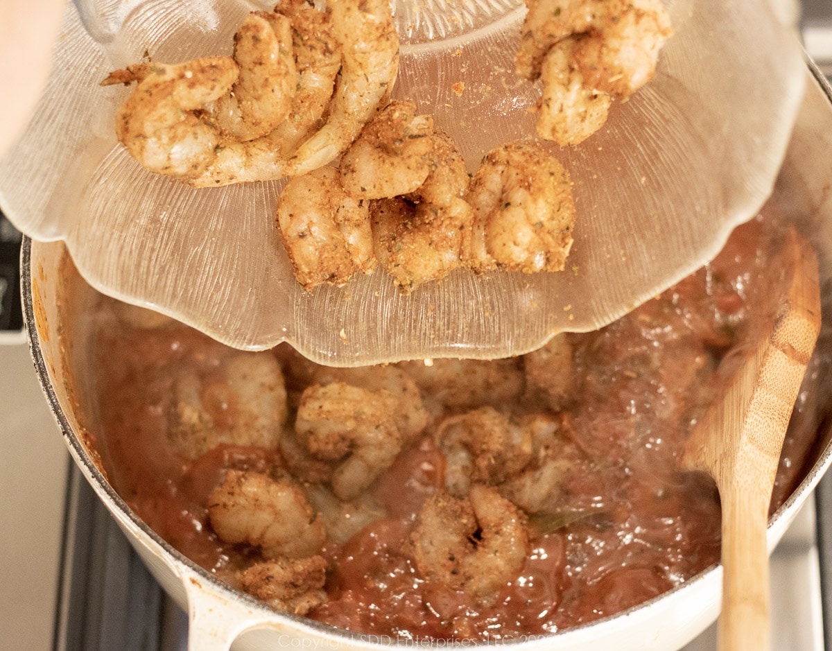 shrimp being placed in sauce in a Dutch oven