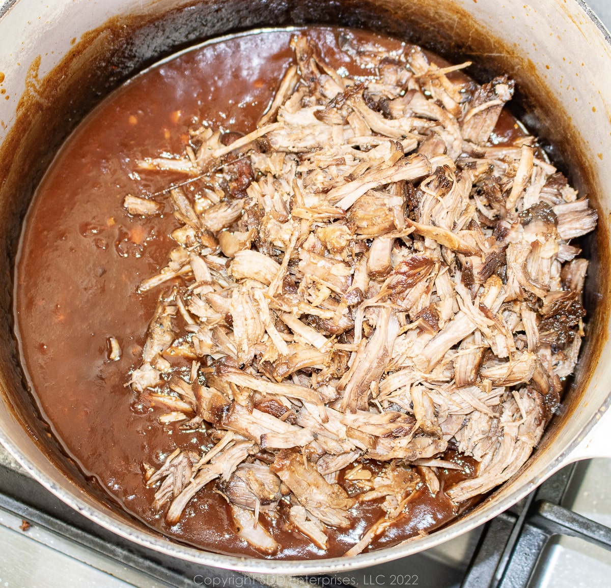 shredded eef added to bbq sauce in a Dutch oven