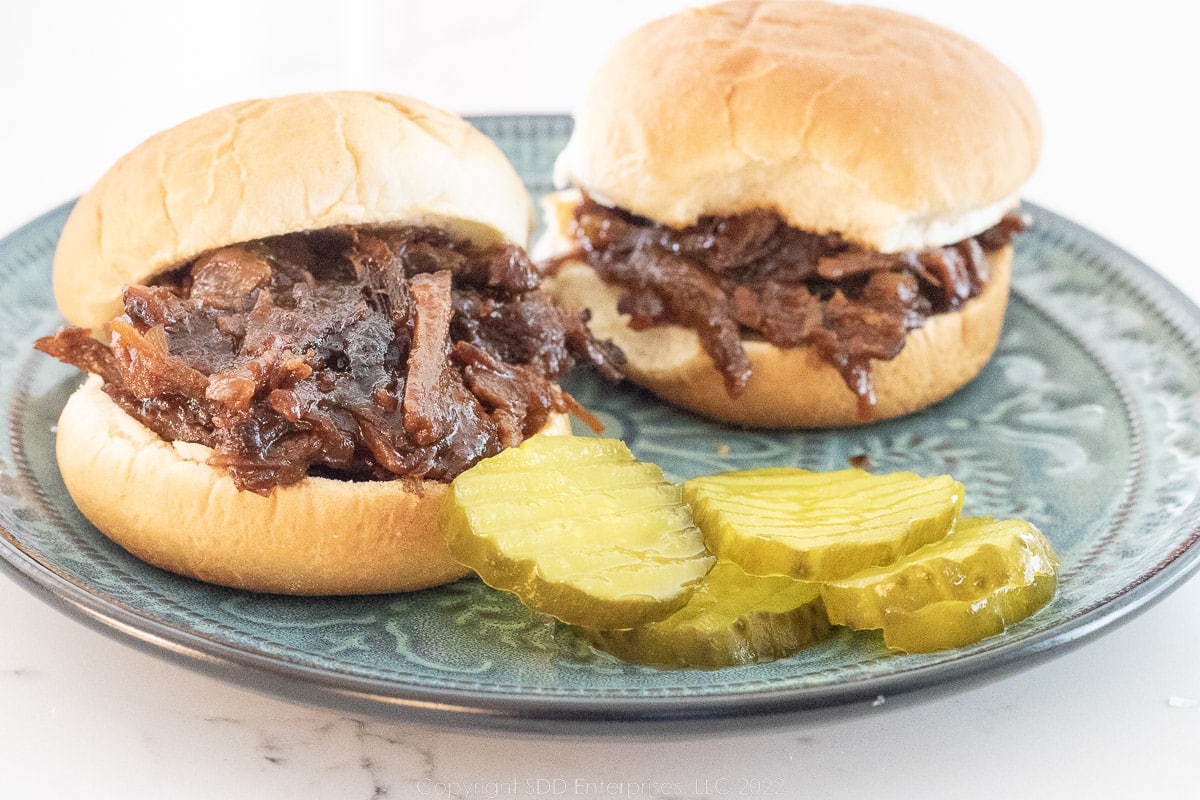 Pulled BBQ beef sliders with pickles on a green plate.