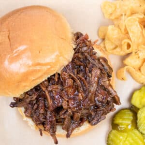 pulled bbq beef sandwich on a bum with pickles and Fritos on the side