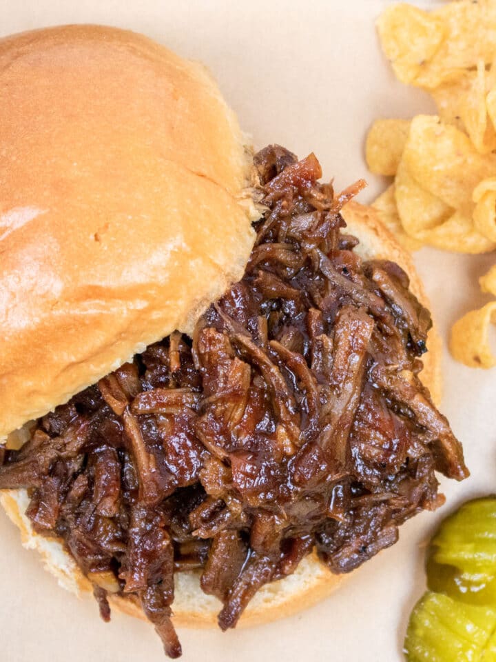 pulled bbq beef sandwich on a bum with pickles and Fritos on the side