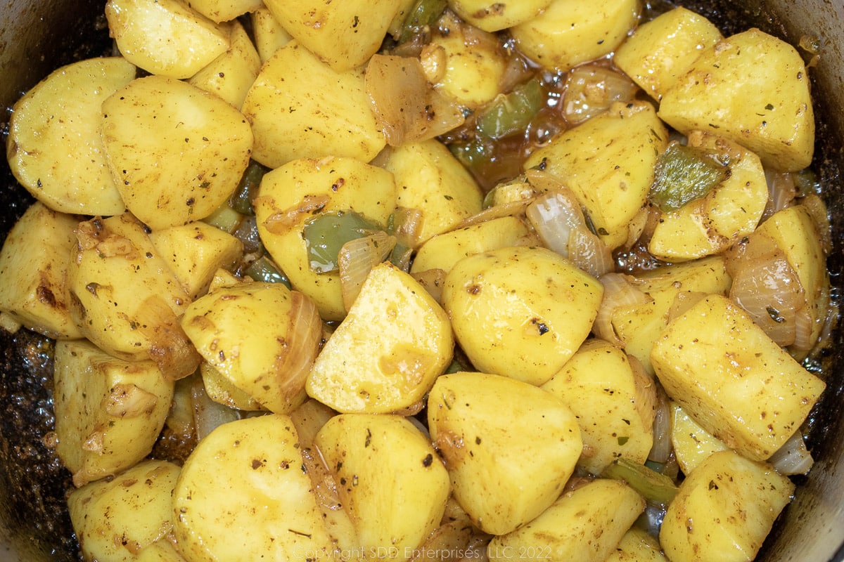 uncooked potatoes mixed with the trinity and seasonings in a Dutch oven