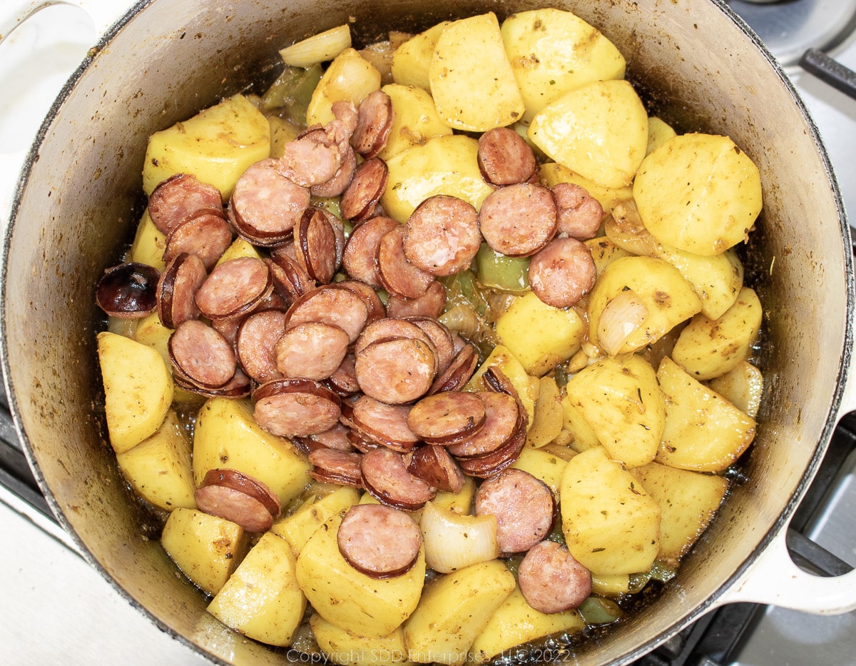 sliced sausage added to the potaoes and trinity in a Dutch oven