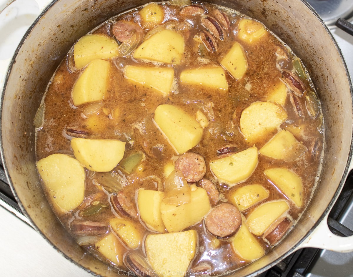 stock added to potaoes and sausage in a Dutch oven