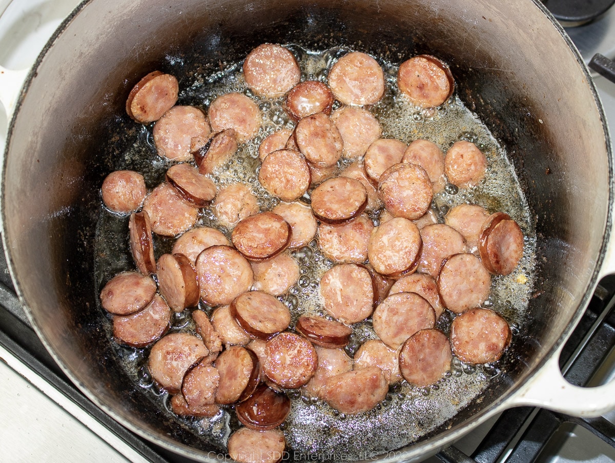 sausage medallions browning in a Dutch oven