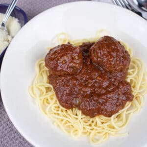 spaghetti and meatballs in a white bowl with parmesan cheese on the side