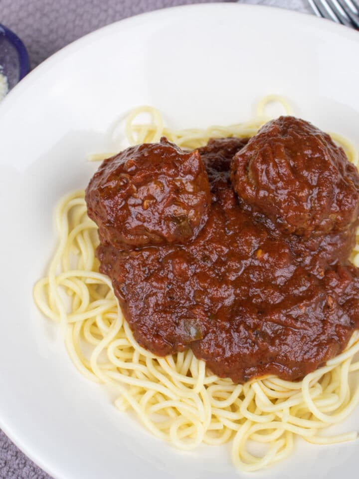 spaghetti and meatballs in a white bowl with parmesan cheese on the side