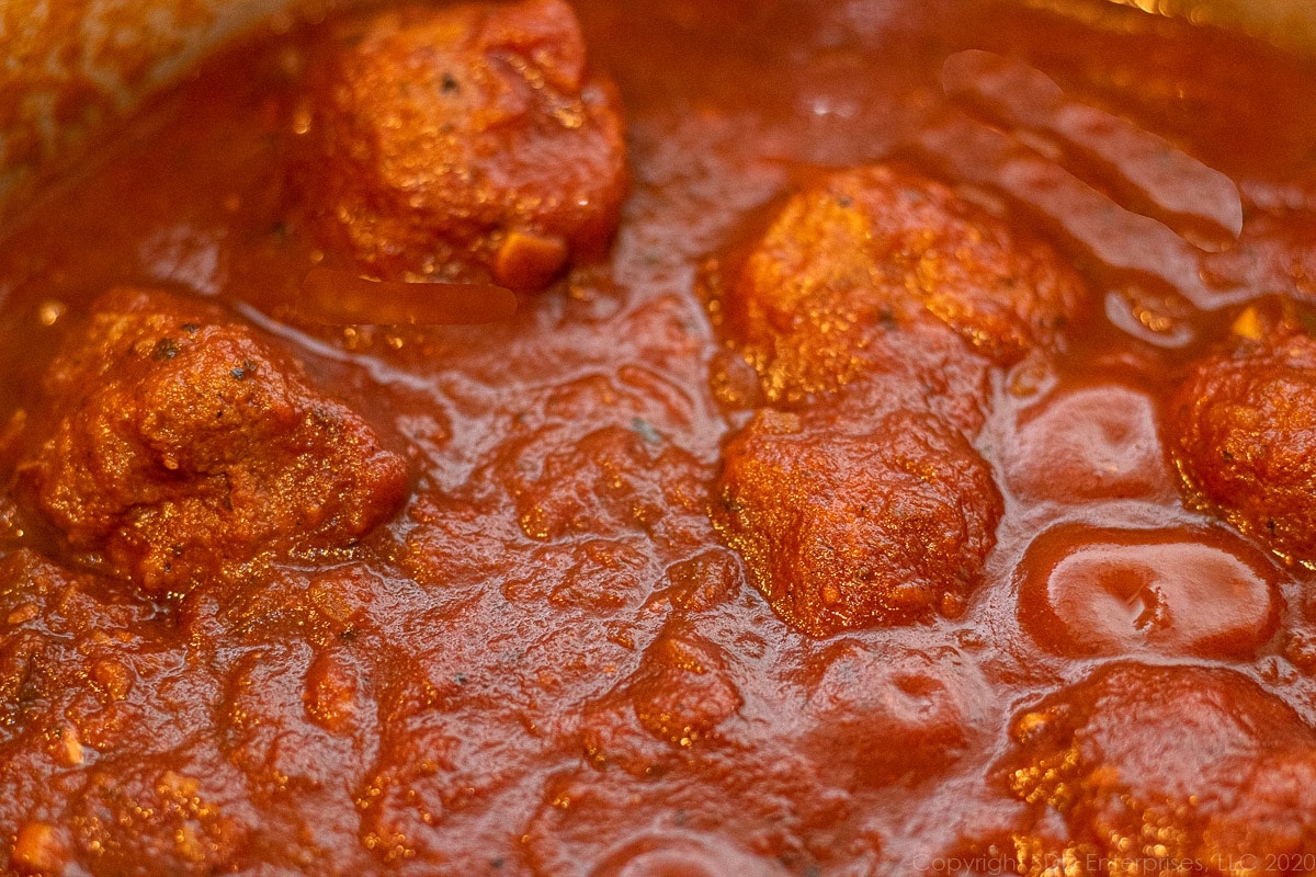 meatballs added to simmering tomato sauce in a Dutch oven