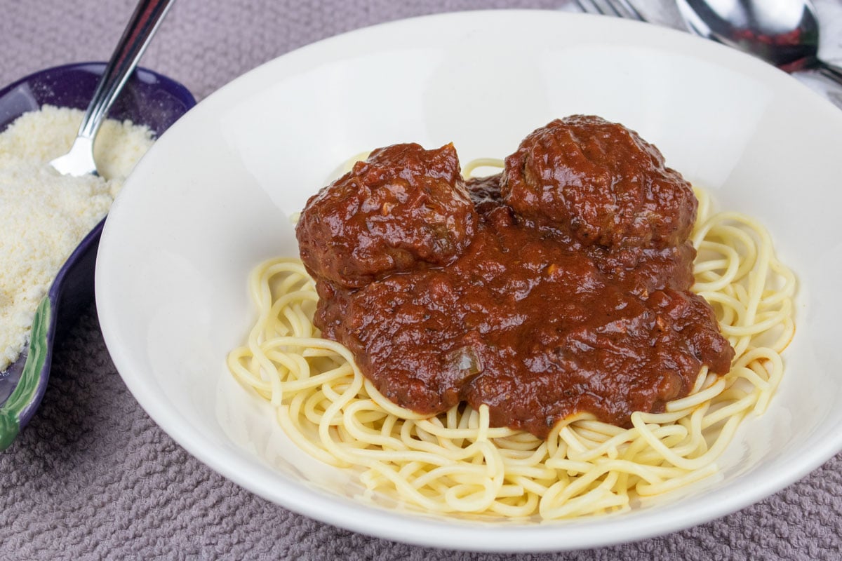 spaghetti and meatballs in a white bowl with parmesan cheese on the side