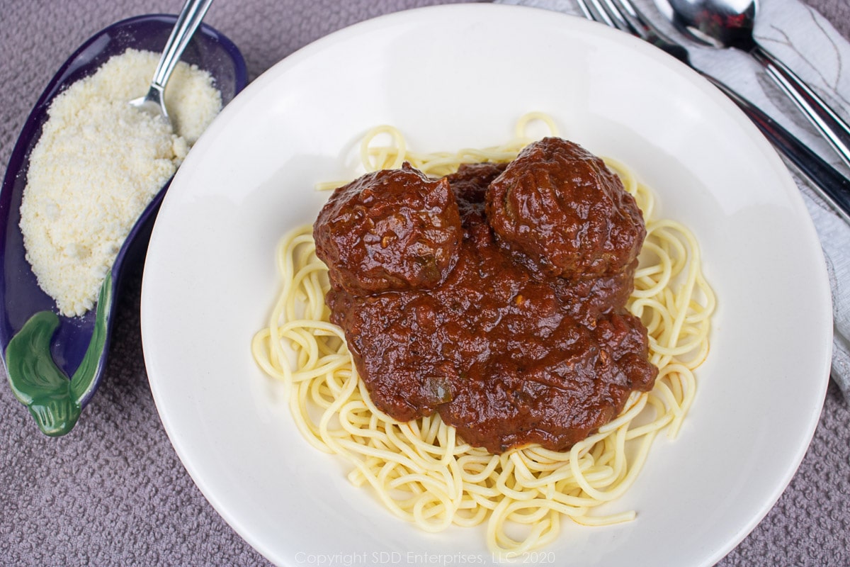 spaghetti and meatballs in a whitebowl with grated cheese on the side