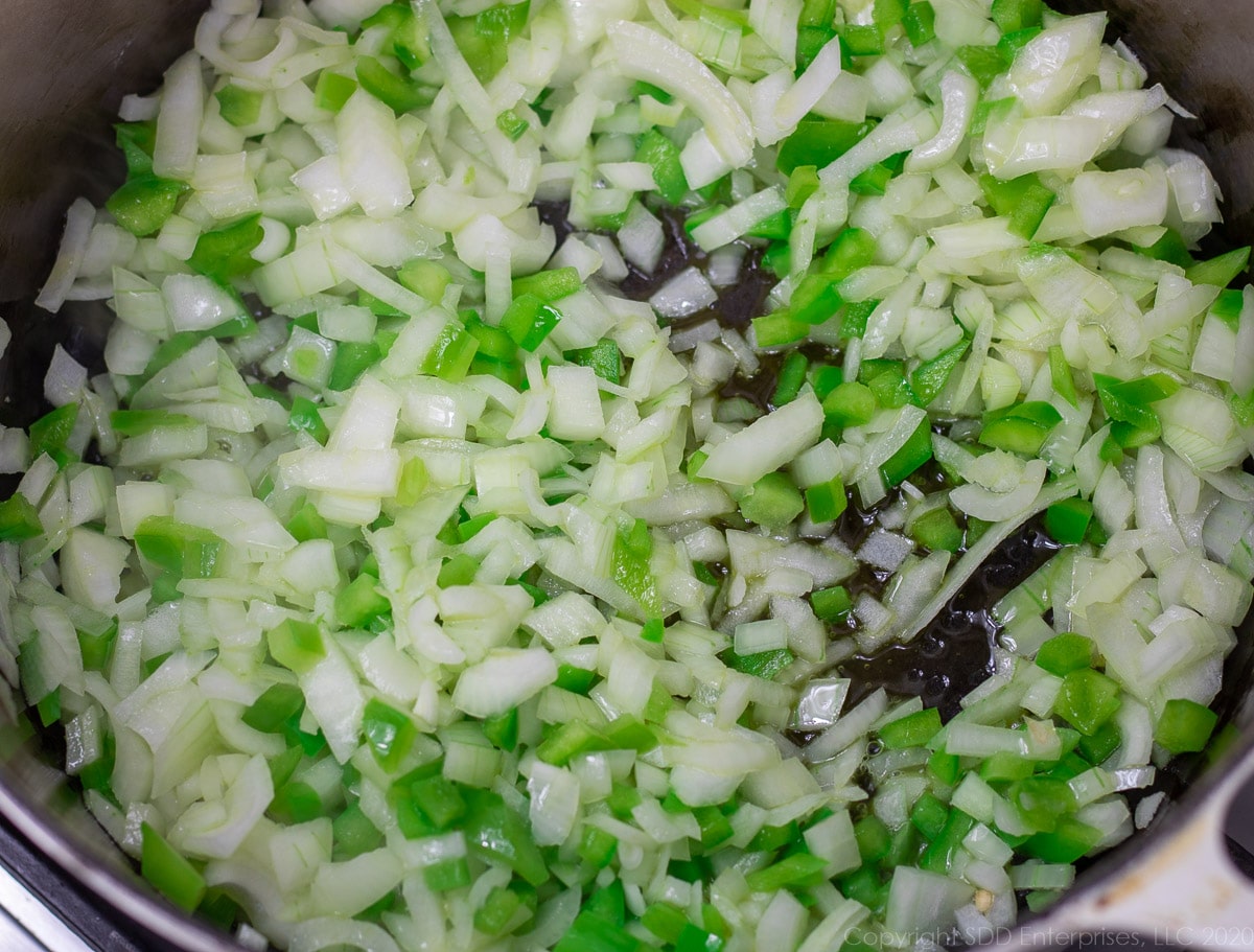 yellow onions and bell peppers sauteing in olive oil in a Dutch oven