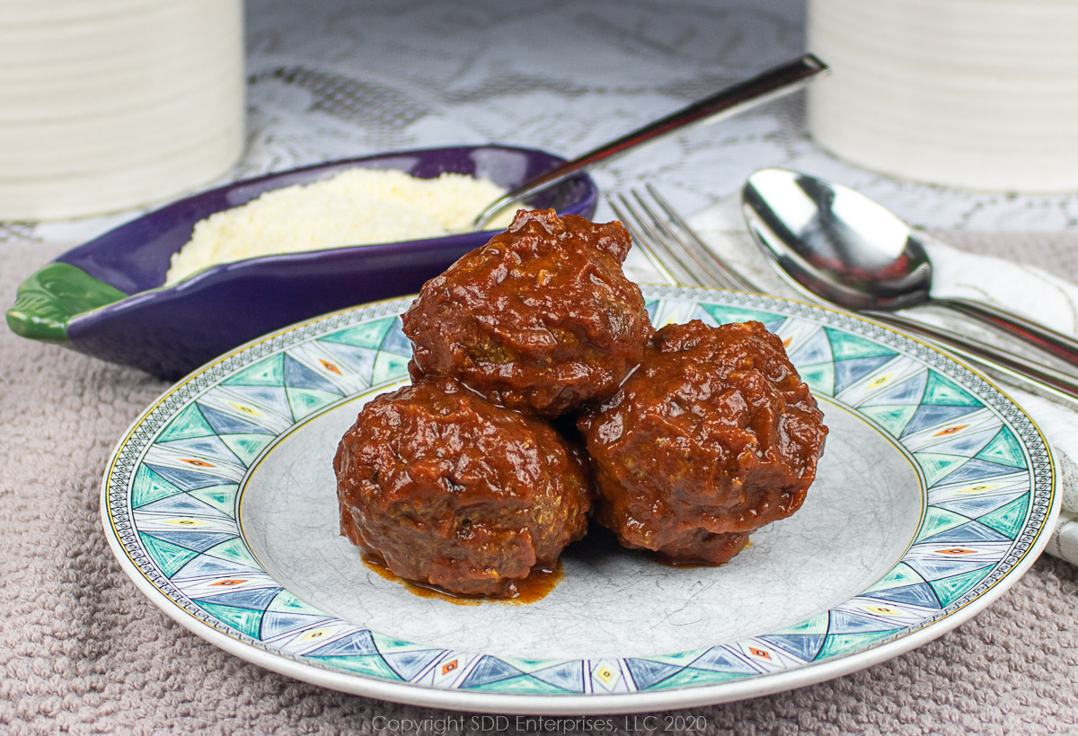 three meatballs on a green and white plate with grated cheese along side