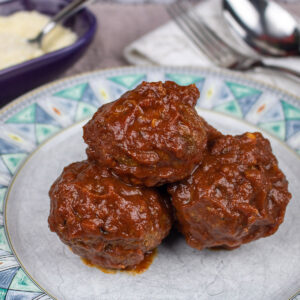 thre meatballs on a green and white plate with grated cheese on side