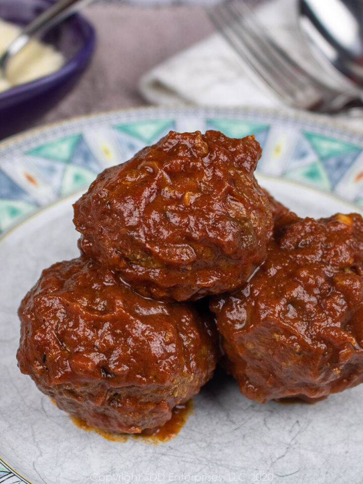 thre meatballs on a green and white plate with grated cheese on side