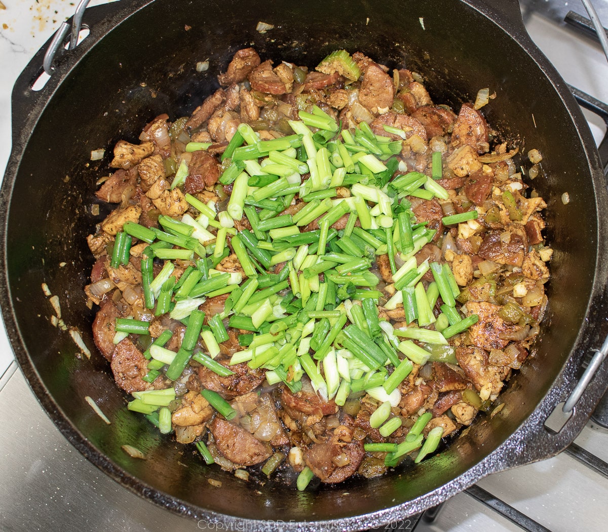sliced green onions added to vegetables and meats in a Dutch oven