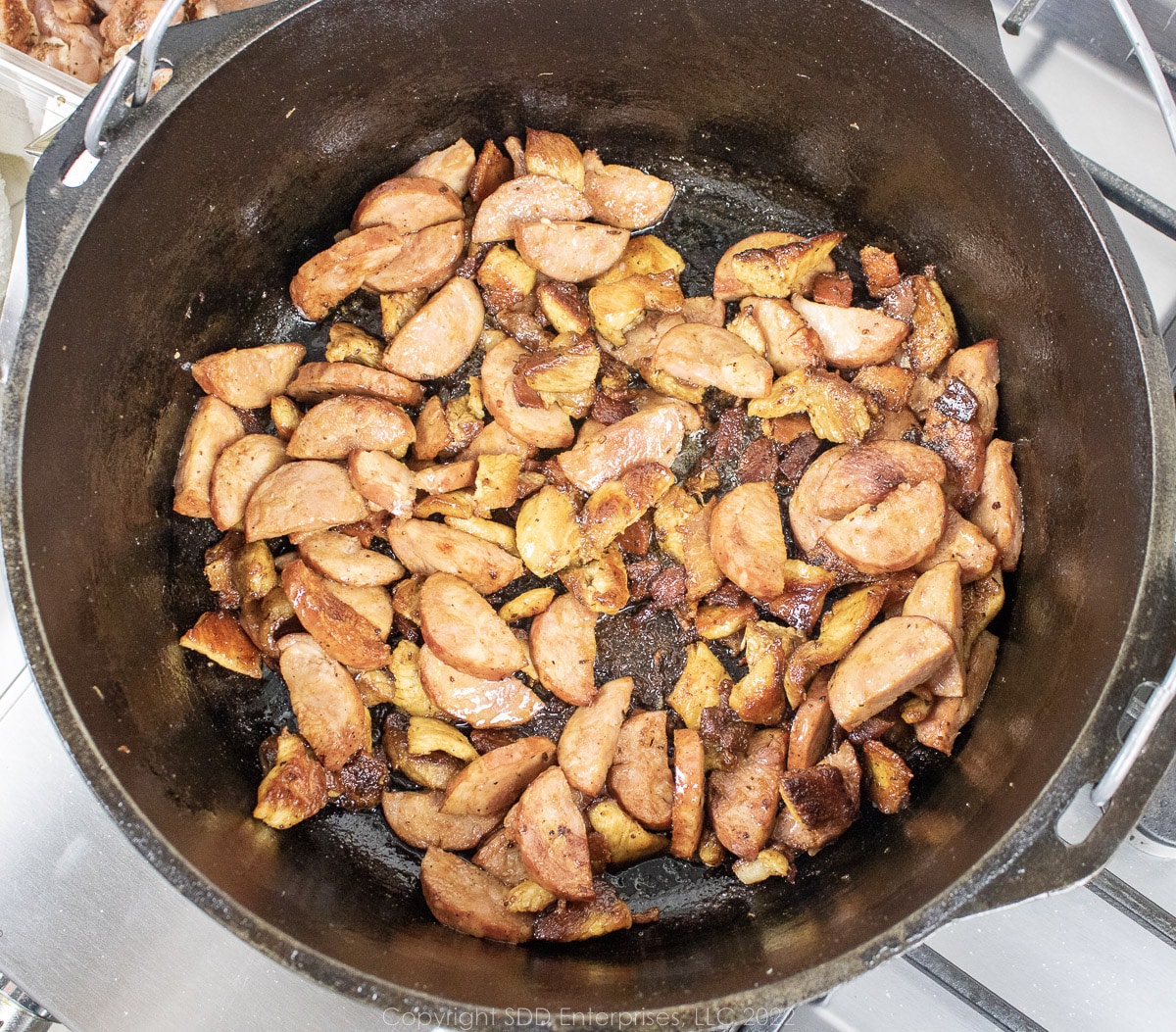 sausage and pork frying in a Dutch oven