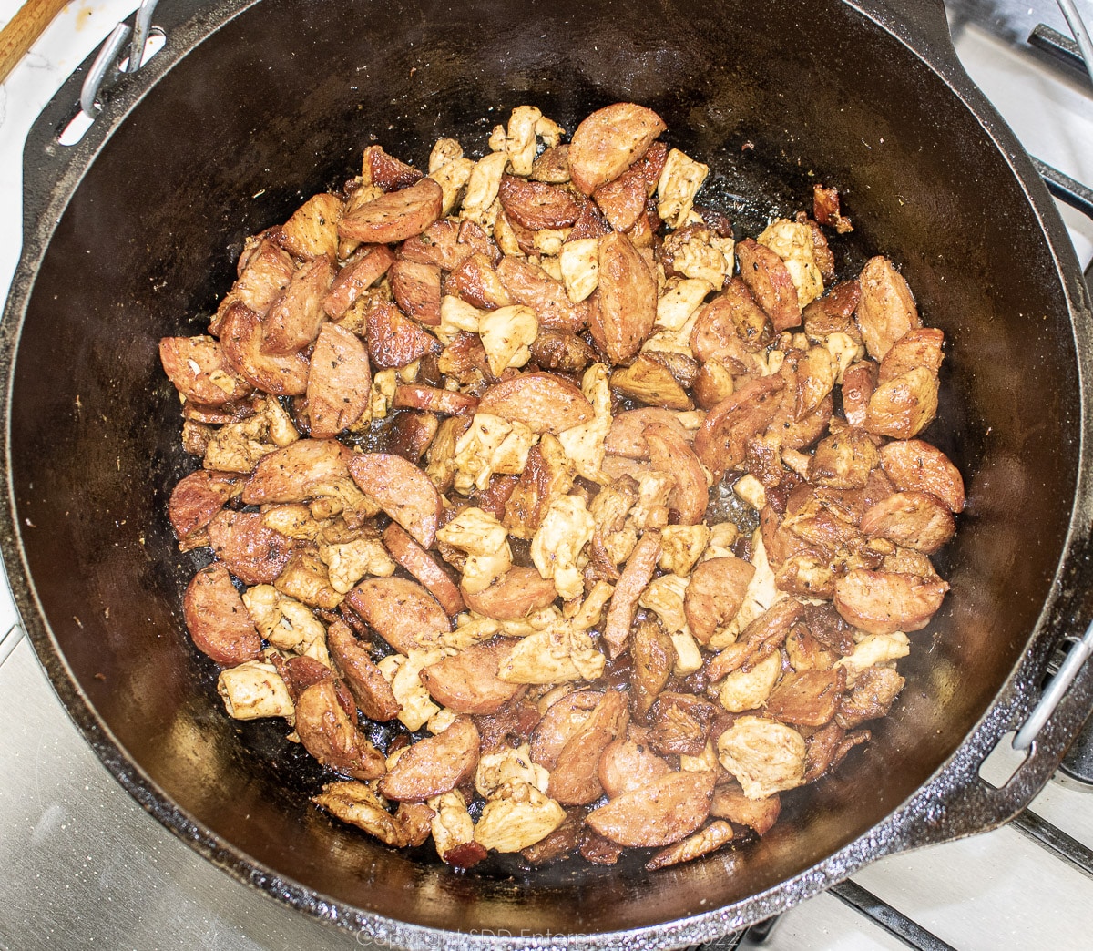 chicken, sausage and pork frying in a Dutch oven