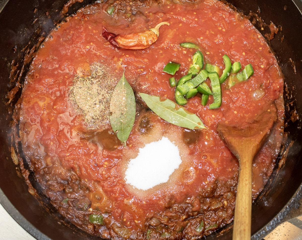 spices and whole tomatoes added to a tomato paste base in a Dutch oven