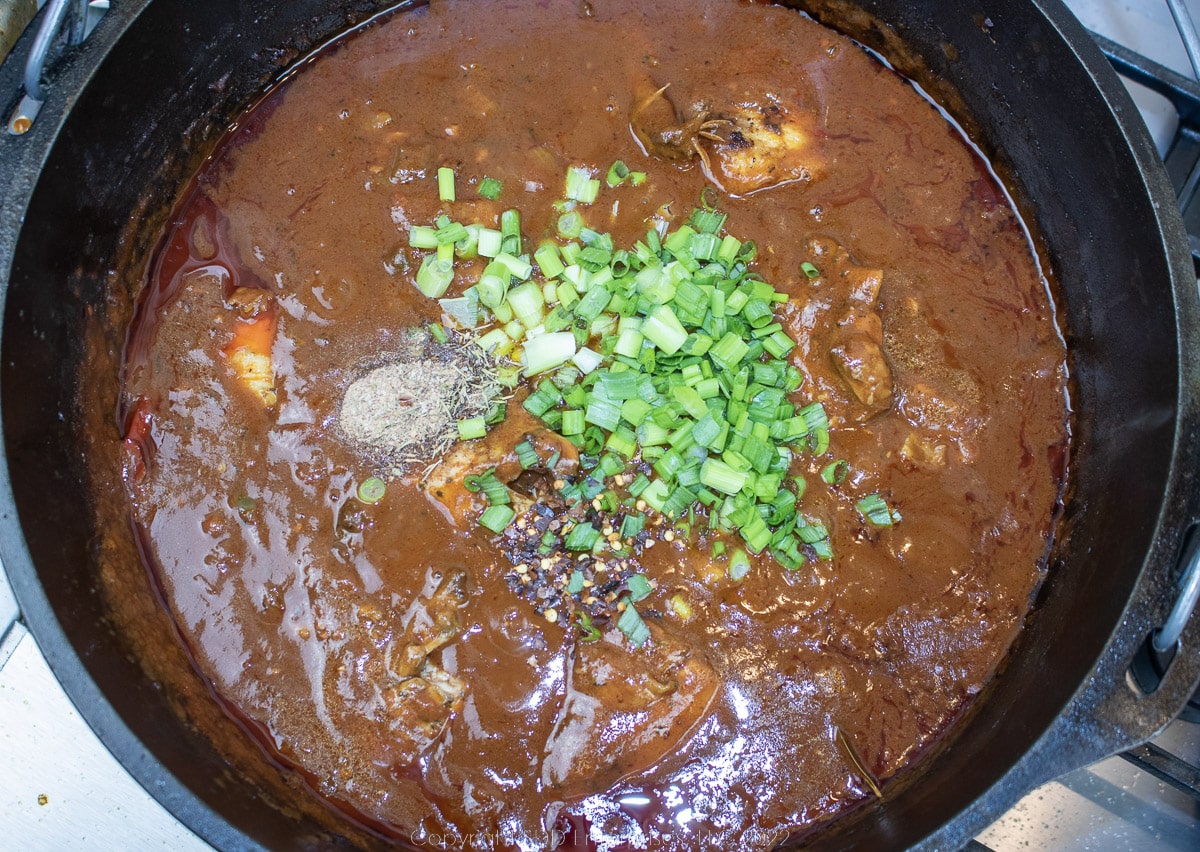 chicken and seasoning added to tomato sauce in a Dutch oven
