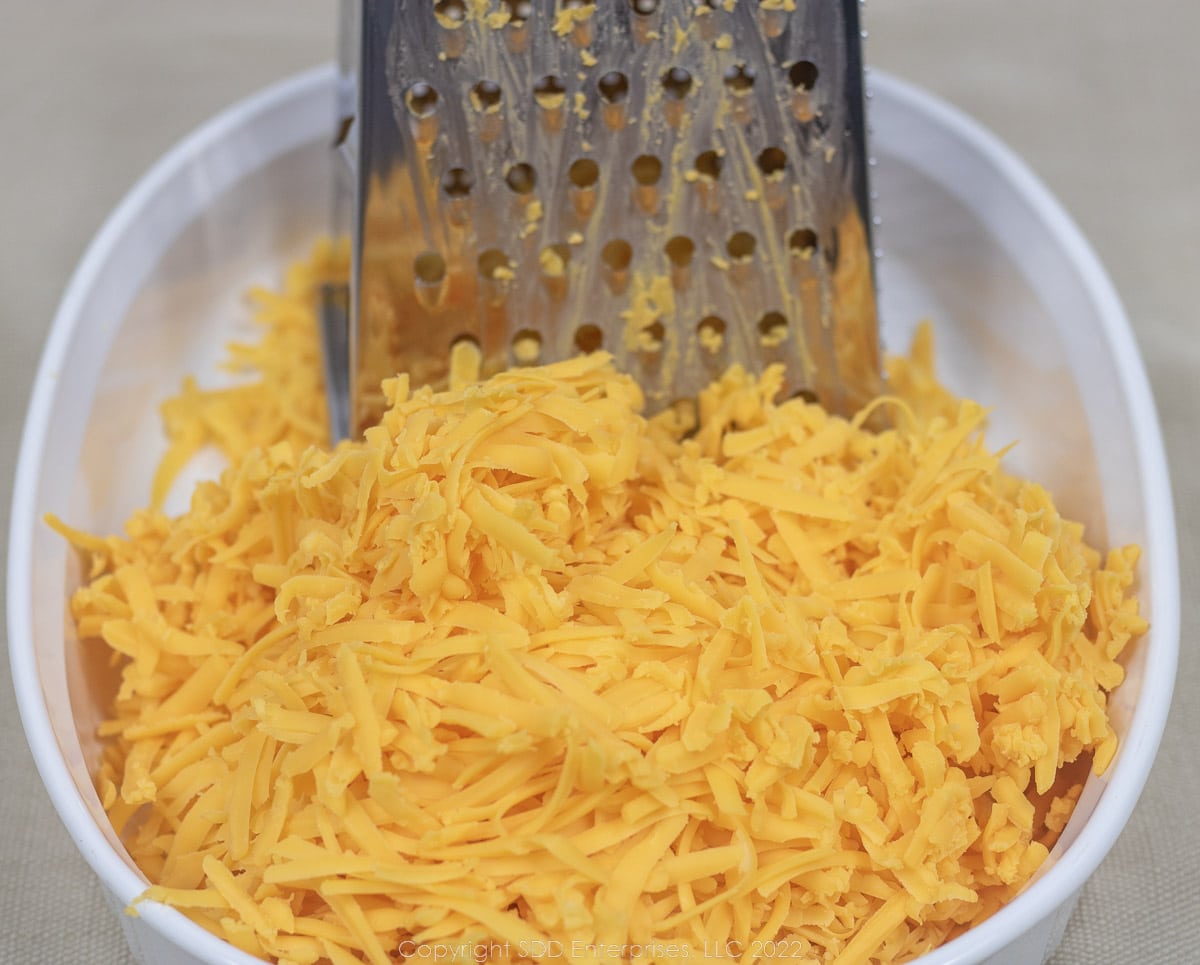 grated cheddar cheese in a white bowl with a grater