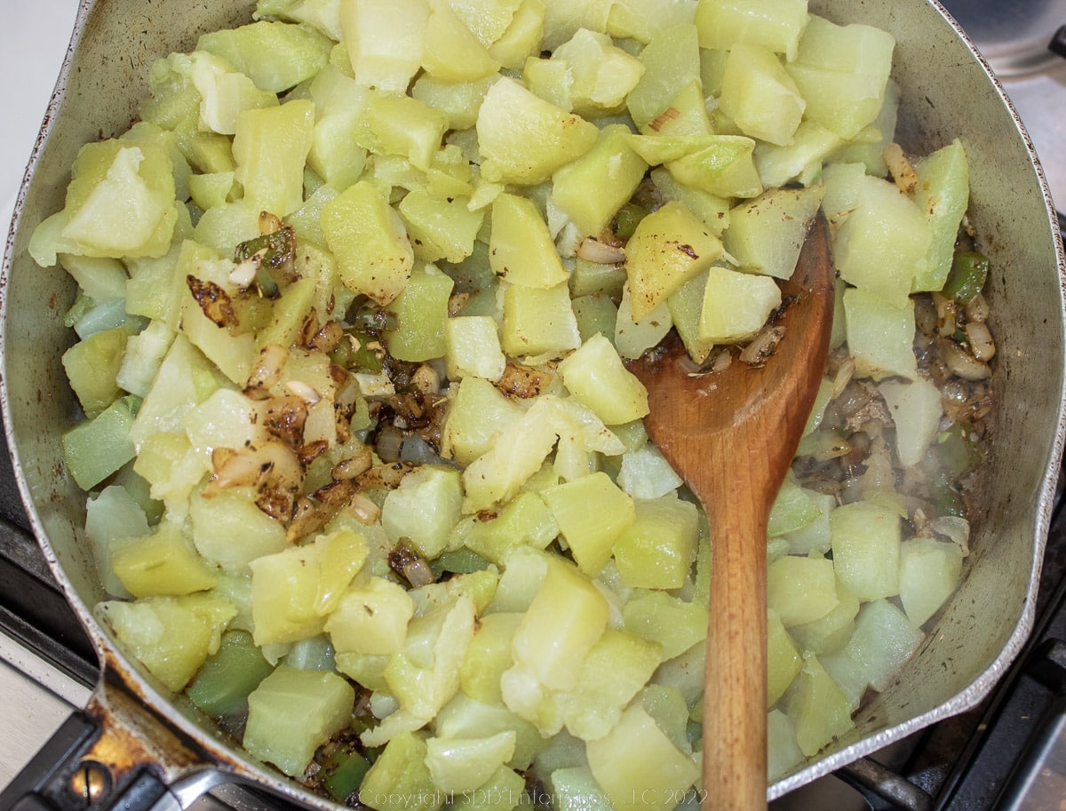 chopped mirliton added to frying vegetables in a frying pan