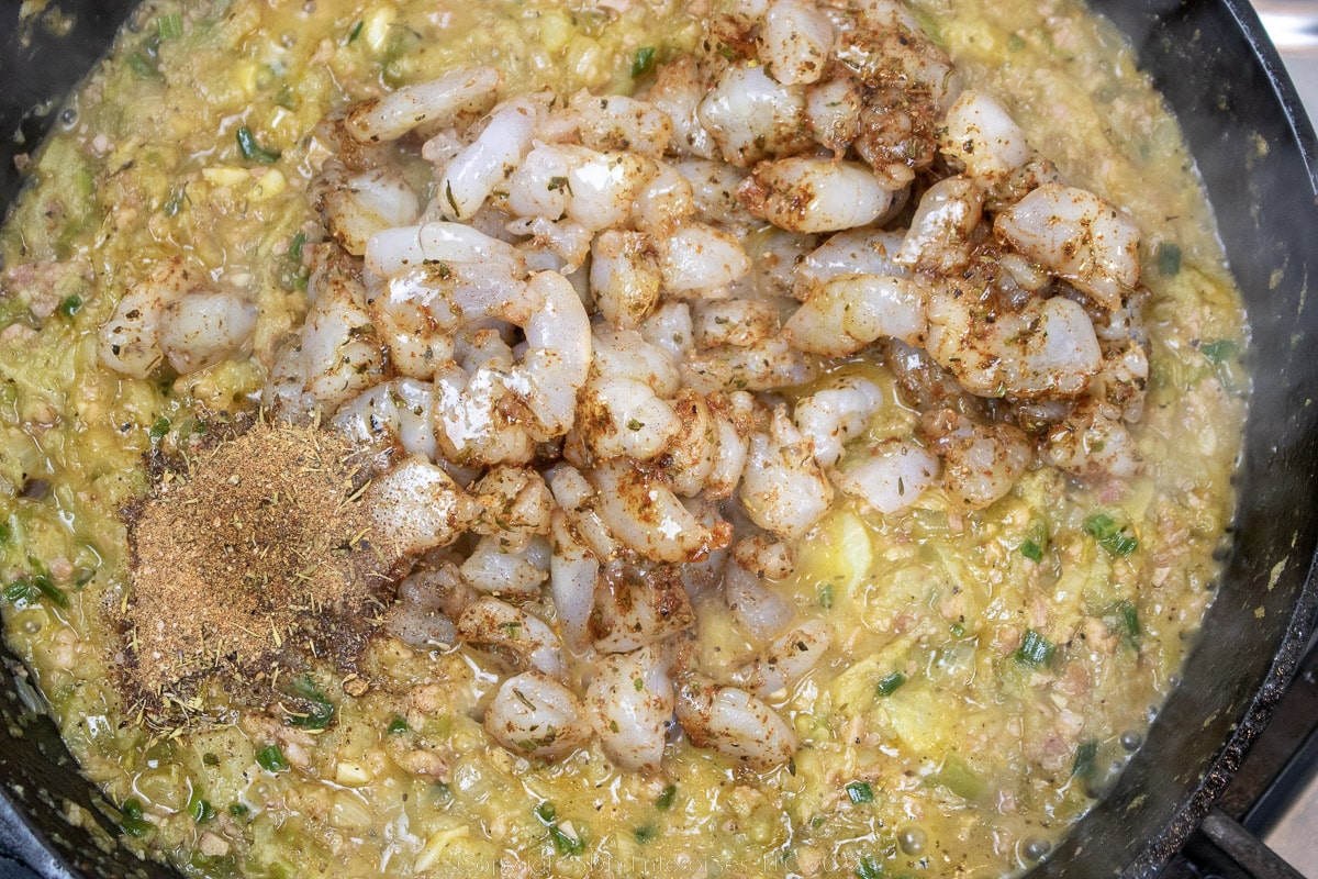 shrimp and seasoning being added to vegetables in a cast iron skillet