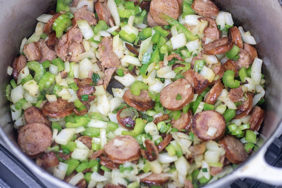 Onions, bell peppers and celery added to a Dutch oven with sausage