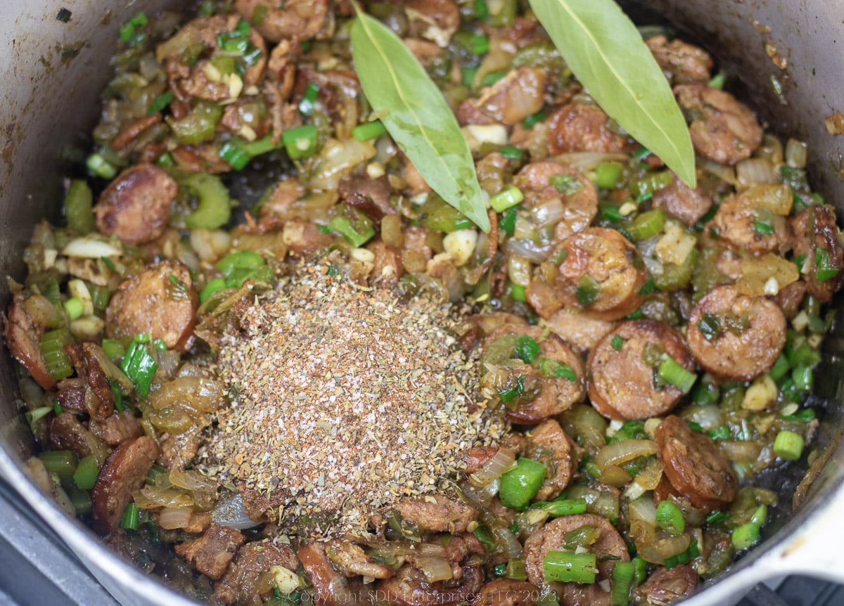 Herbs and spices added to sautéing vegetables and sausage in a Dutch oven