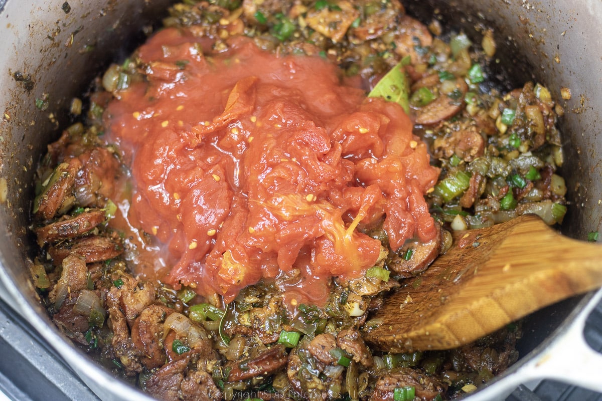 whole tomatoes mixed into a vegetable-sausage mix in a Dutch oven