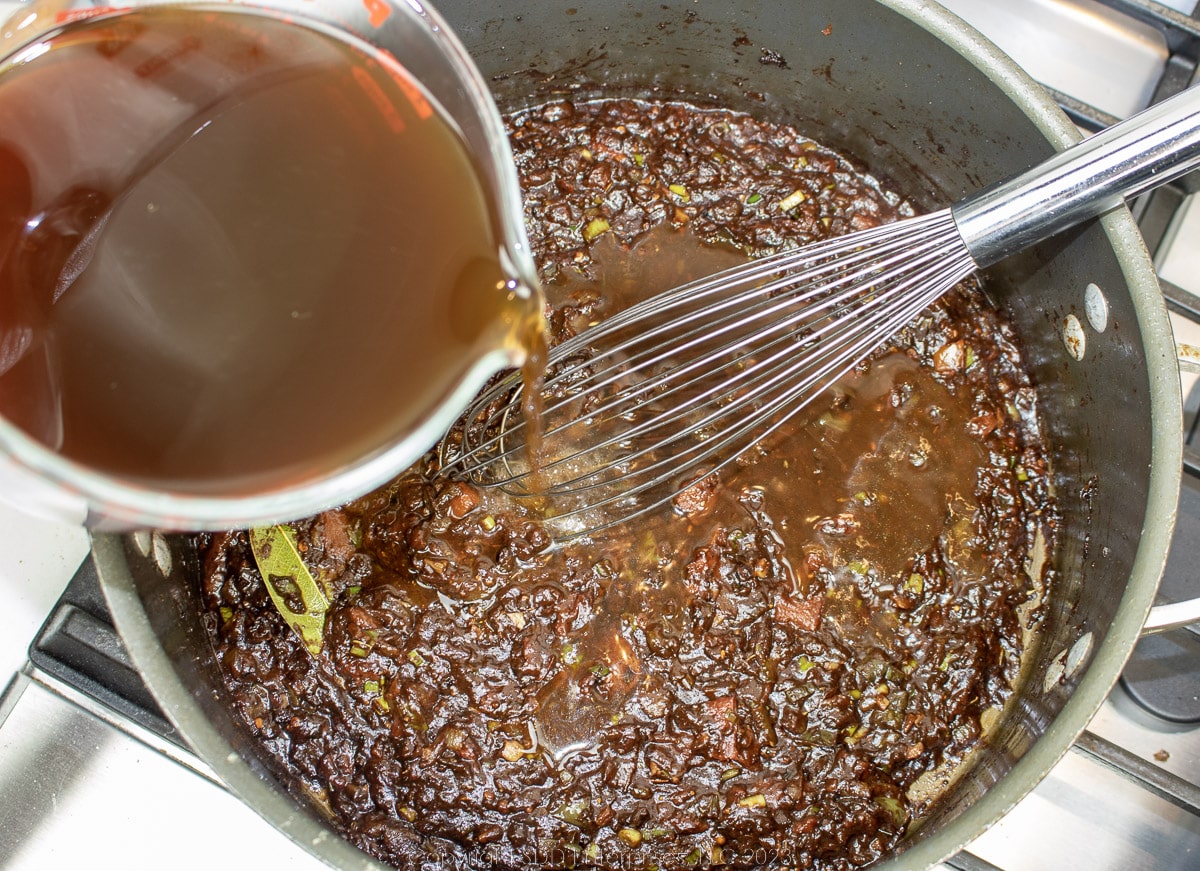 adding stock to a tomato base in a dutch oven