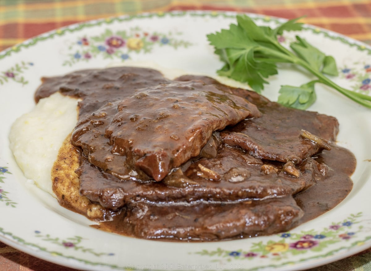 grillades with gravy over grits on a plate with garnish