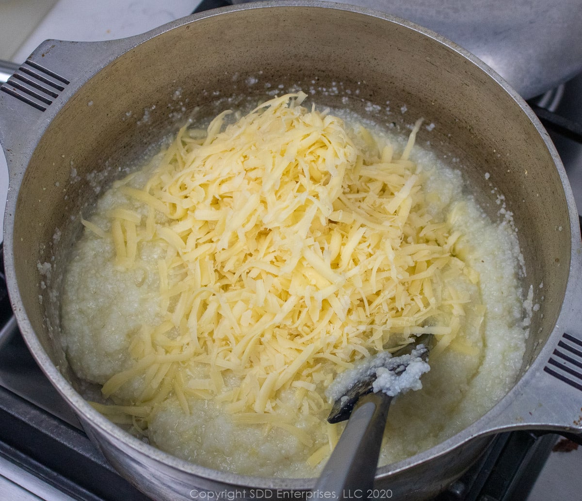 gruyere cheese being added to grits in a Dutch oven